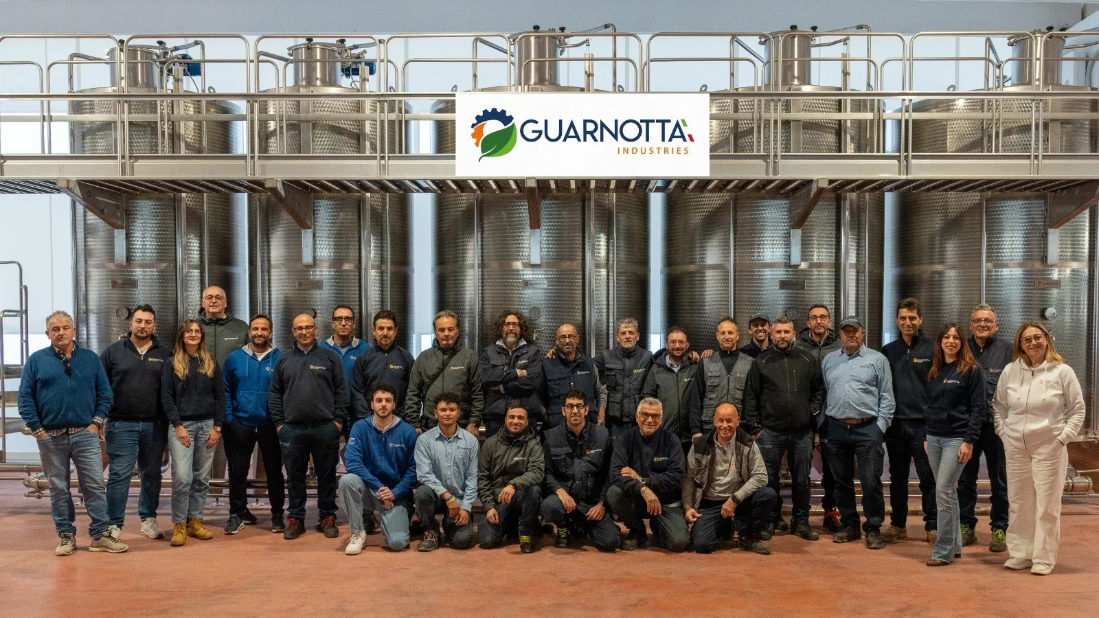 La squadra Guarnotta Industries davanti a una fila di serbatoi inox con passerella